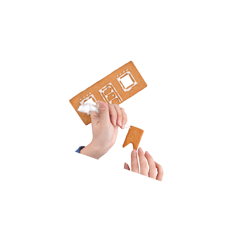 Young woman is decorating Christmas Gingerbread House cookies biscuit at home with frosting topping in icing bag, close up, lifestyle.